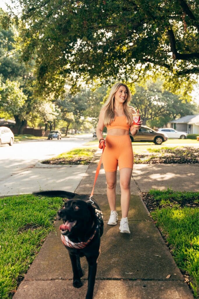 A woman walking her dog while holding a smoothie from Smoothie King on the go