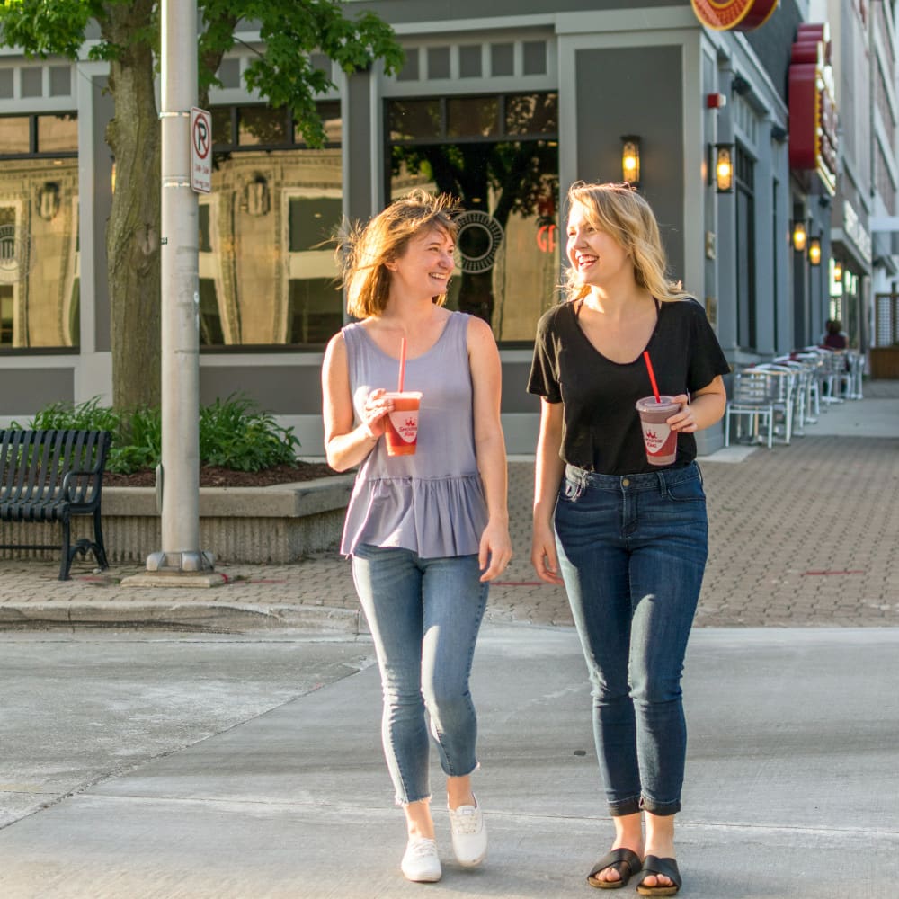 Two women walking across a street in the city with Smoothie King smoothies
