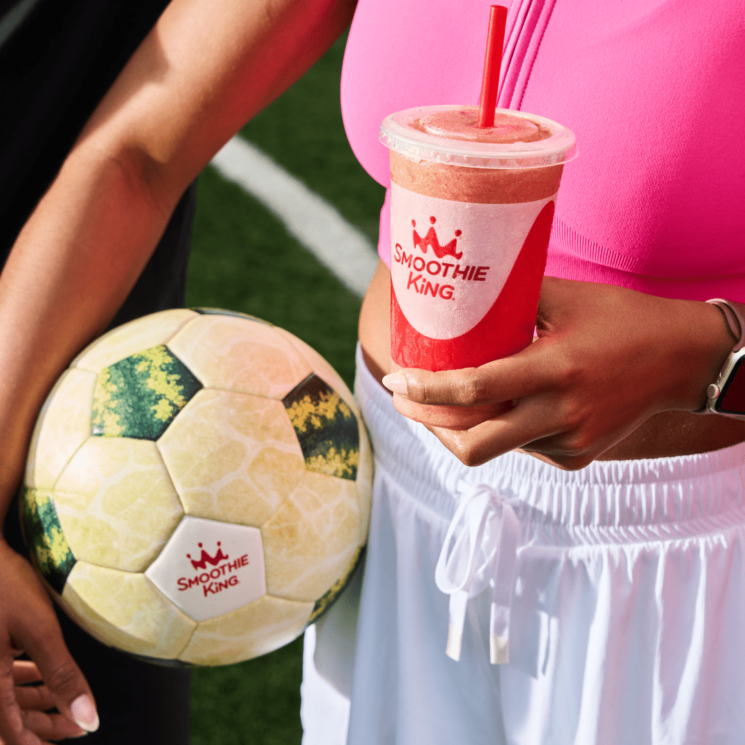 A woman holding a Smoothie King watermelon smoothie and a soccer ball